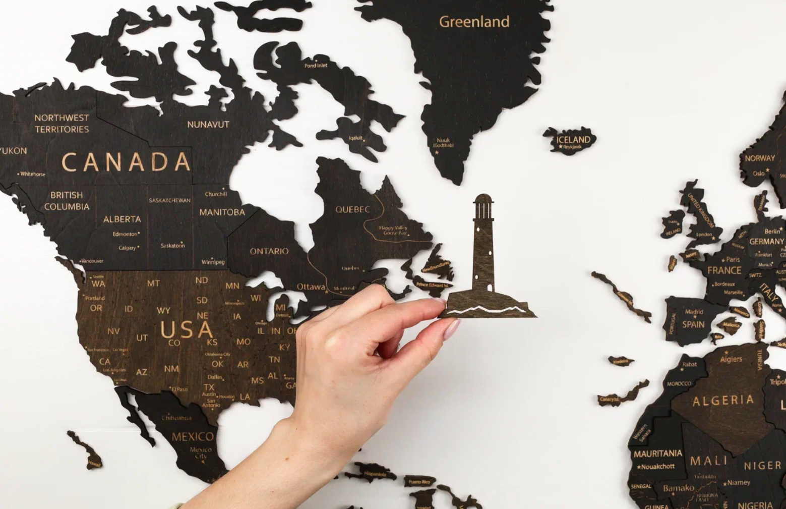 Person adding a wooden lighthouse decoration to a completed Pinelini 3D wooden world map